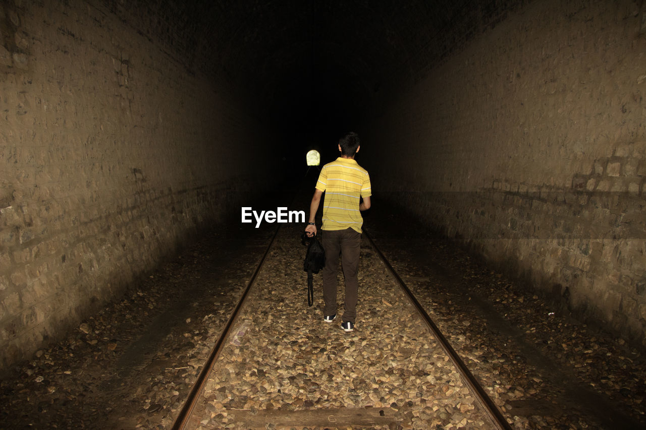 REAR VIEW OF A PERSON WALKING IN TUNNEL