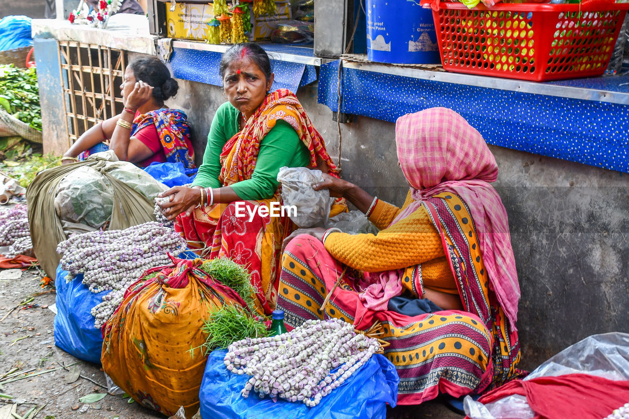 FULL LENGTH OF FRIENDS SITTING IN TRADITIONAL CLOTHING