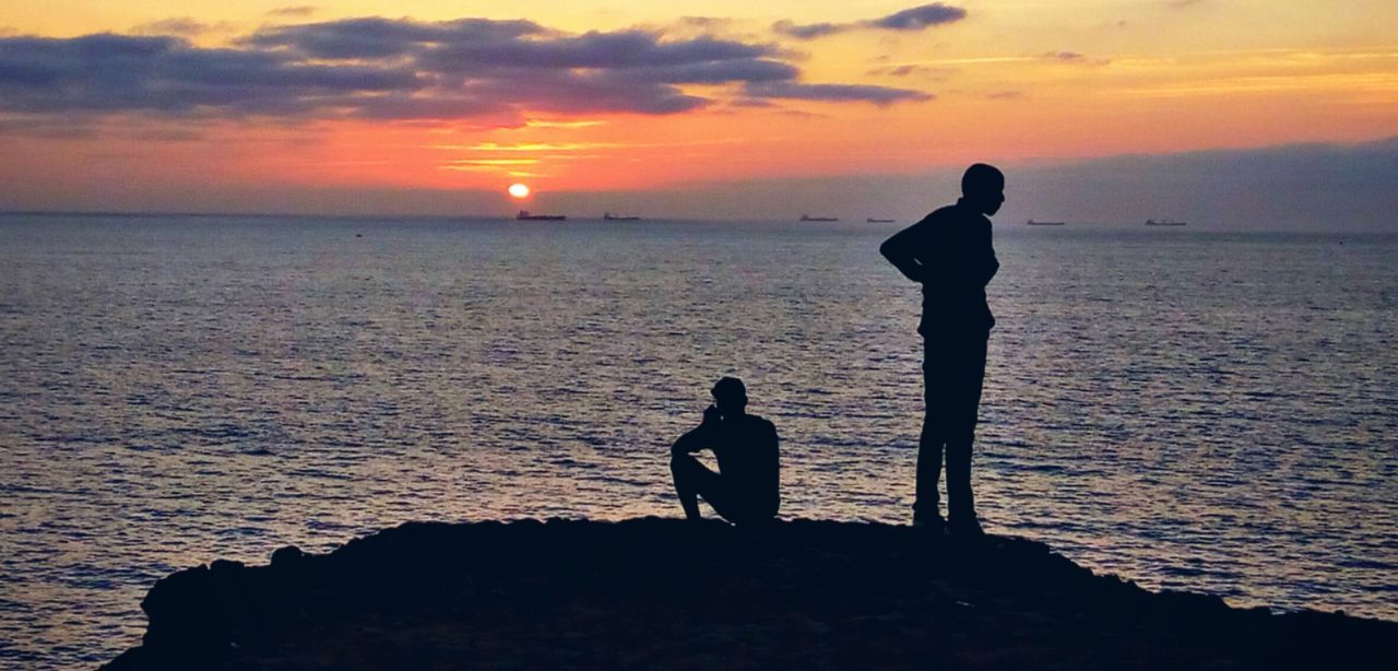 Silhouette people standing at beach against sky during sunset