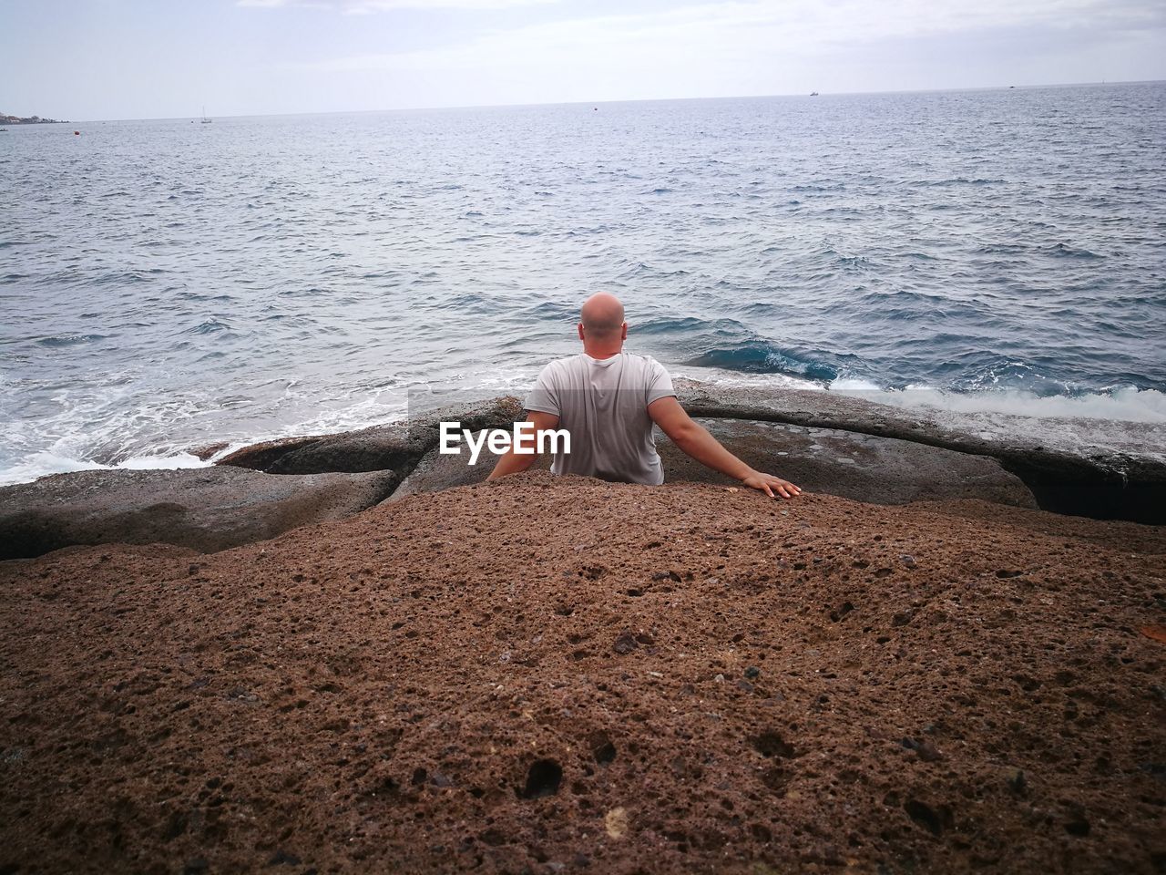 Rear view of man looking at sea while sitting on rock