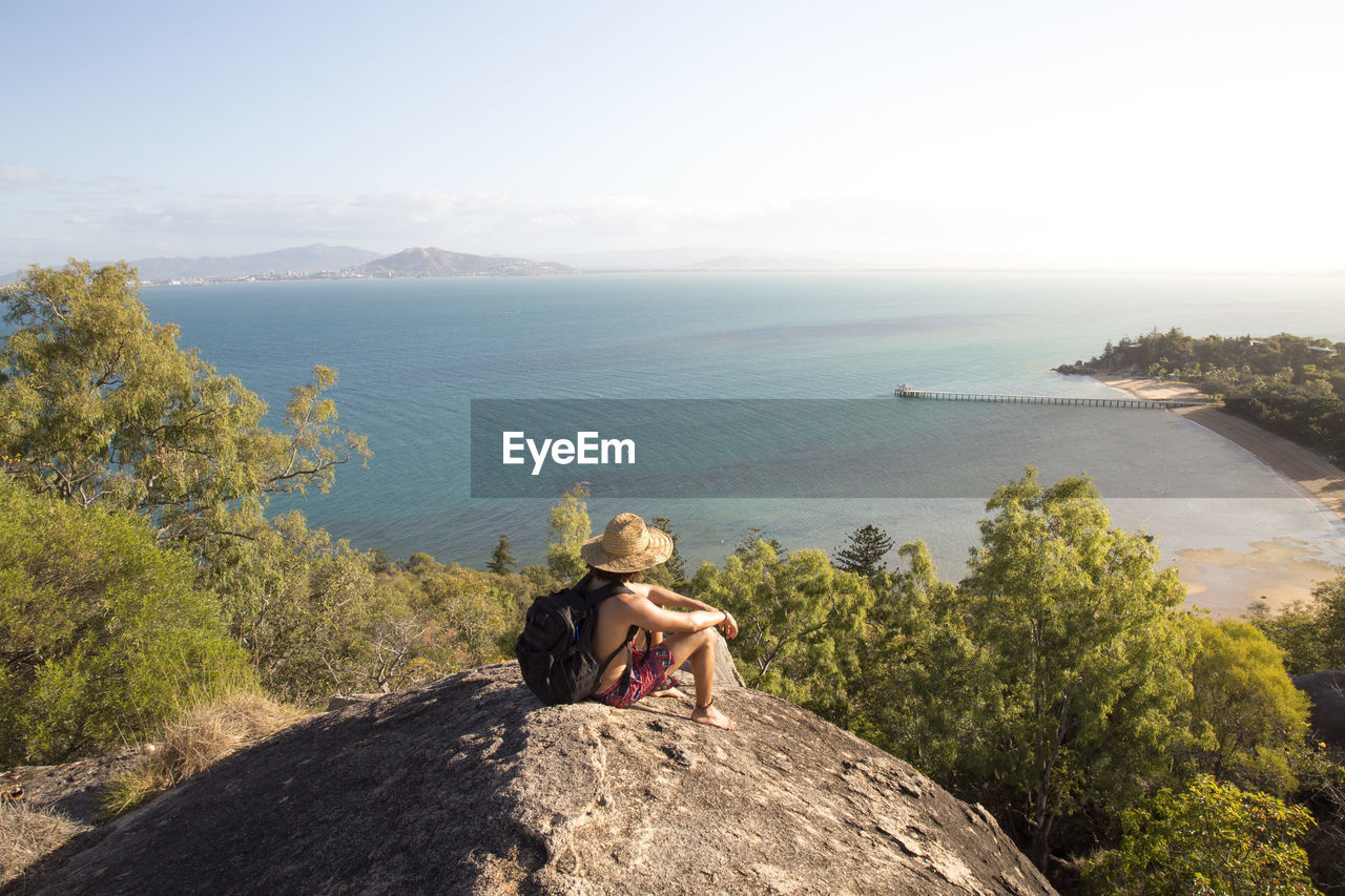 Backpacker with hat and swimsuit, on top of rocky hill during sunset