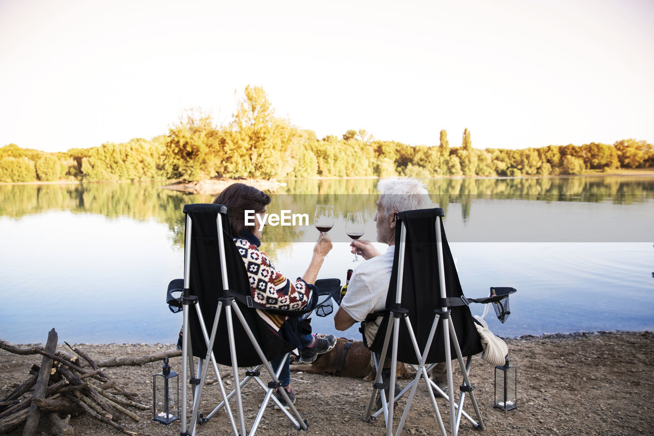 Senior couple clinking wine glasses at a lake in the evening