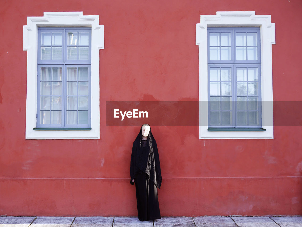 Woman wearing burka standing against red building
