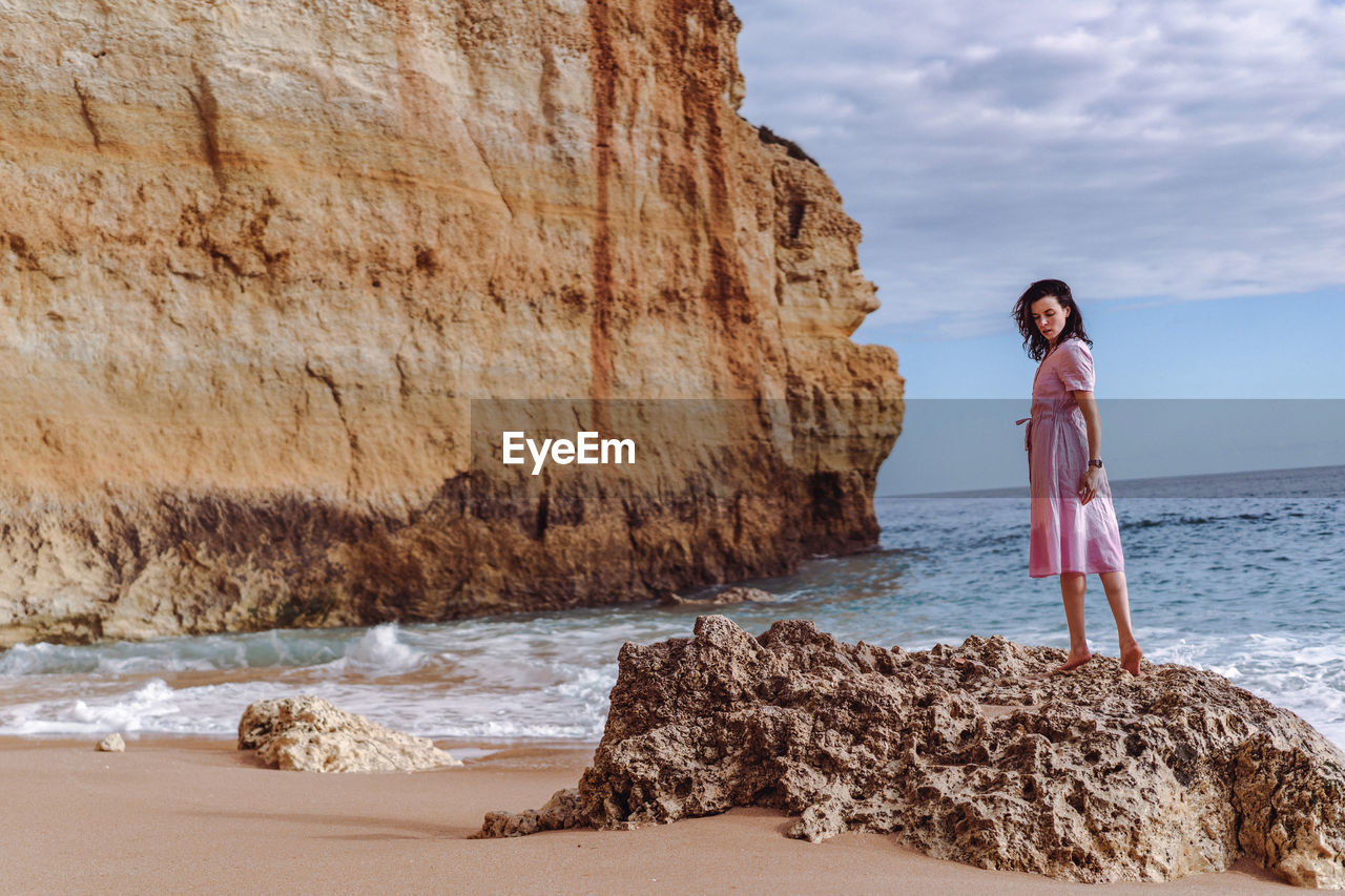 Woman standing on rock at beach against sky