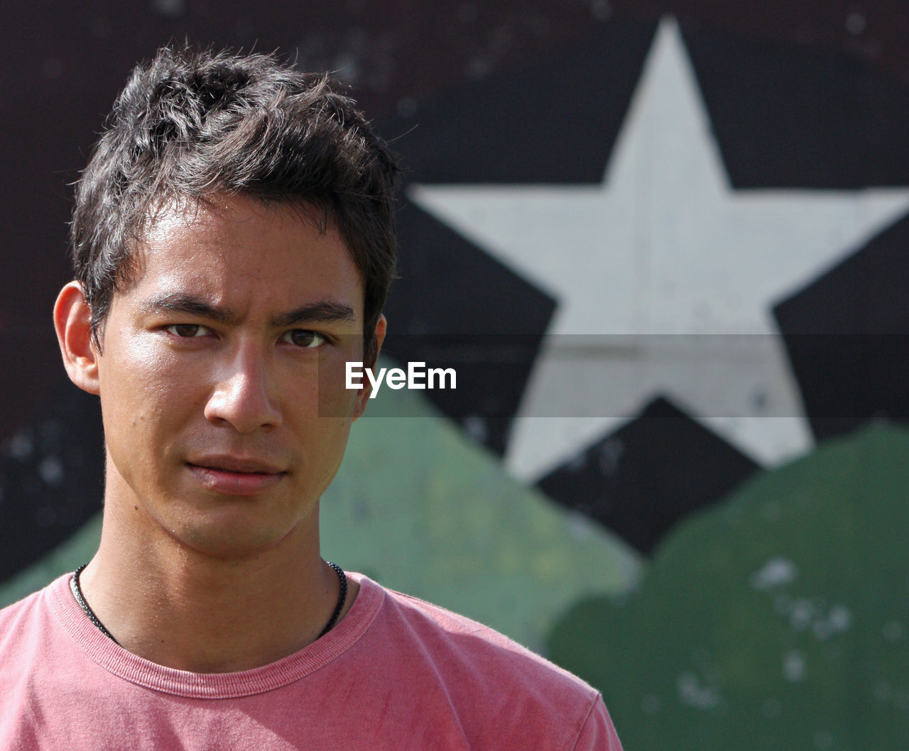 Young eurasian adult looking into the camera with a serious look in front of a wall with a star.