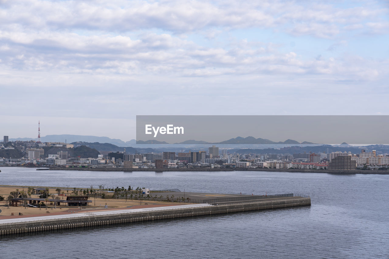 View of buildings by river against cloudy sky