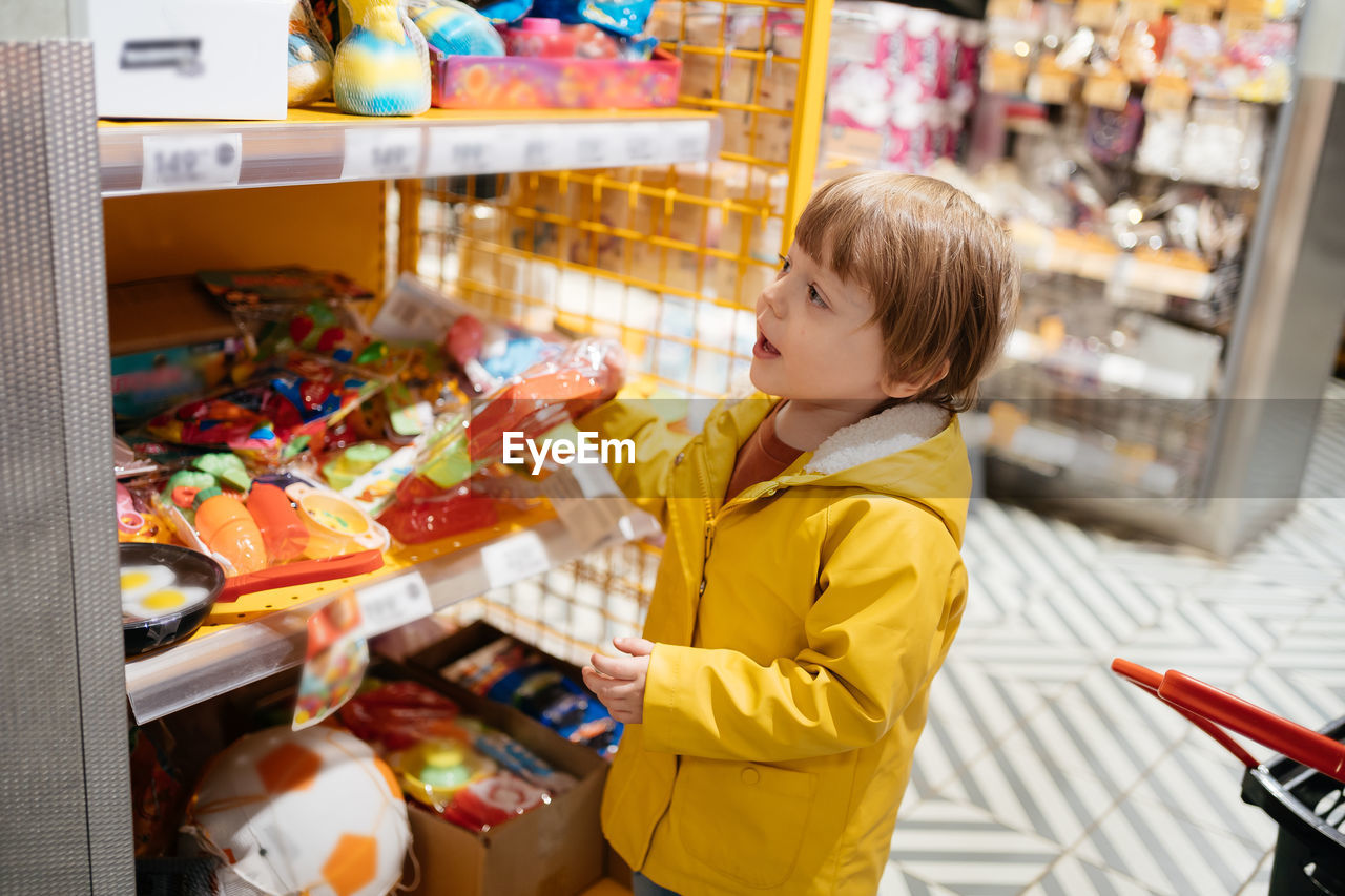 childhood, child, one person, supermarket, retail, store, grocery store, food, men, indoors, food and drink, shopping, side view, standing, groceries, variation, consumerism, looking, choosing, casual clothing, blond hair, customer, toddler, lifestyles, market, holding, innocence, business, waist up, cute, shelf, person