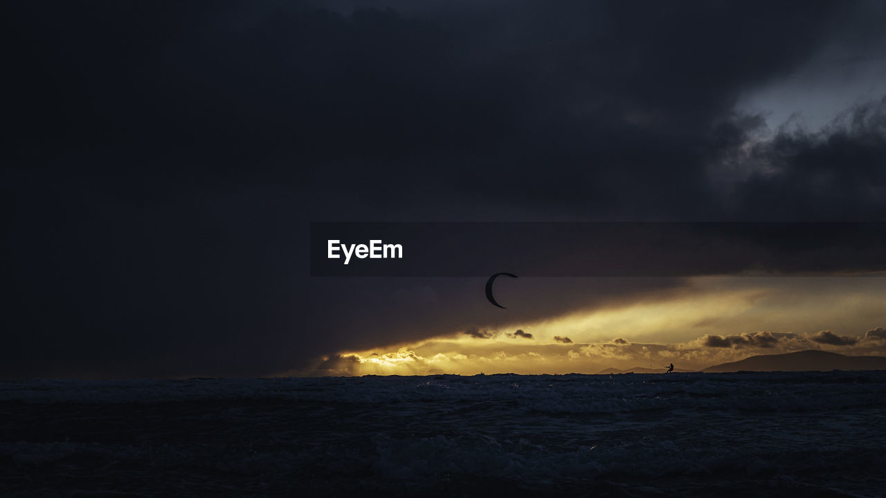 A kitesurfer in high winds surf's in a storm at sunset/sunrise. reeks district, kerry, ireland.