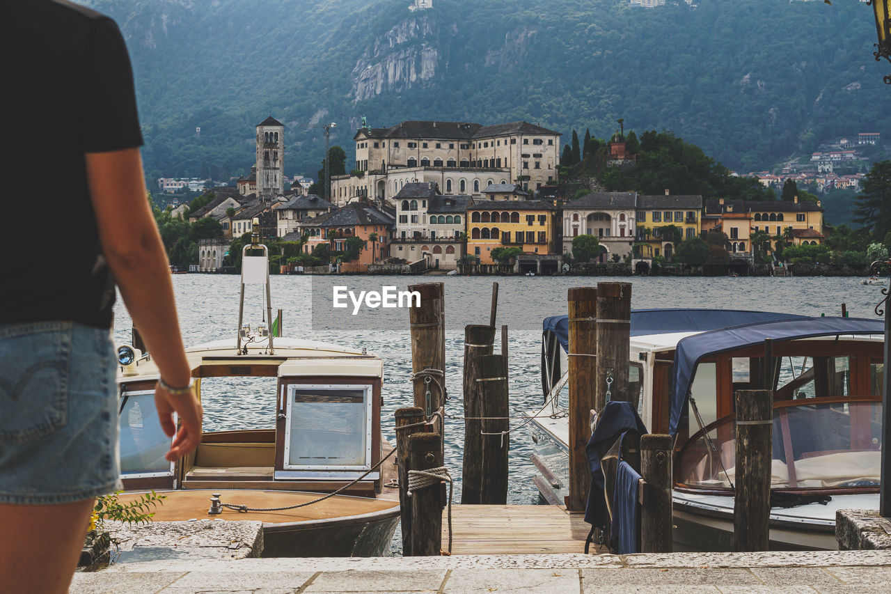 Rear view of man standing by lake against boat and orta san giulio island