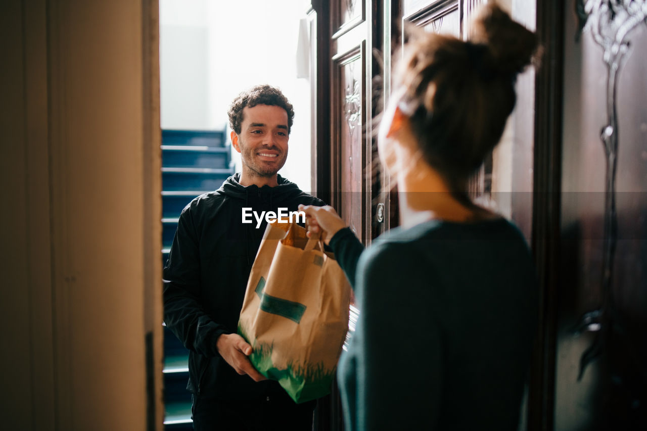 Smiling delivery man delivering bag to woman standing at doorway