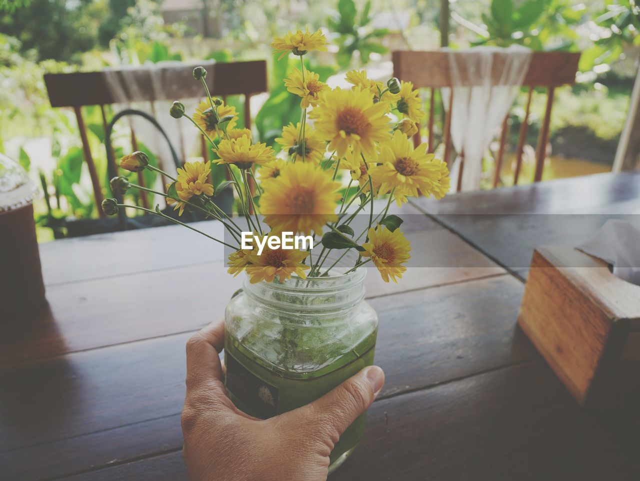MIDSECTION OF PERSON HOLDING YELLOW FLOWERING PLANT ON TABLE