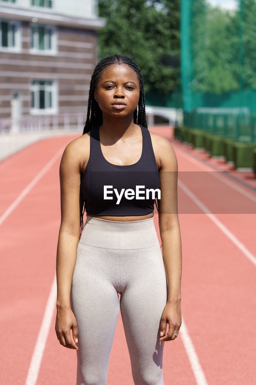 African american sportswoman stands against blurry running track preparing for run on sunny day