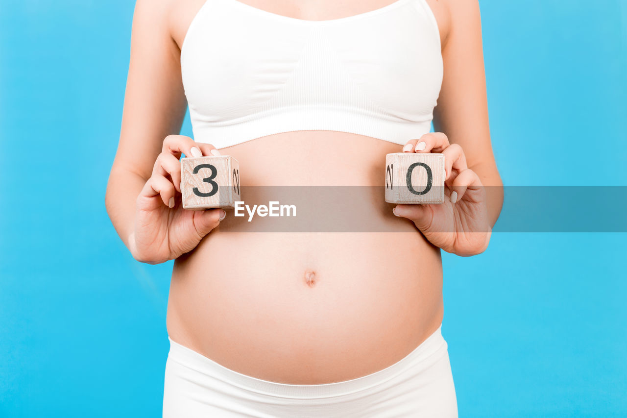 MIDSECTION OF WOMAN STANDING AGAINST BLUE SKY