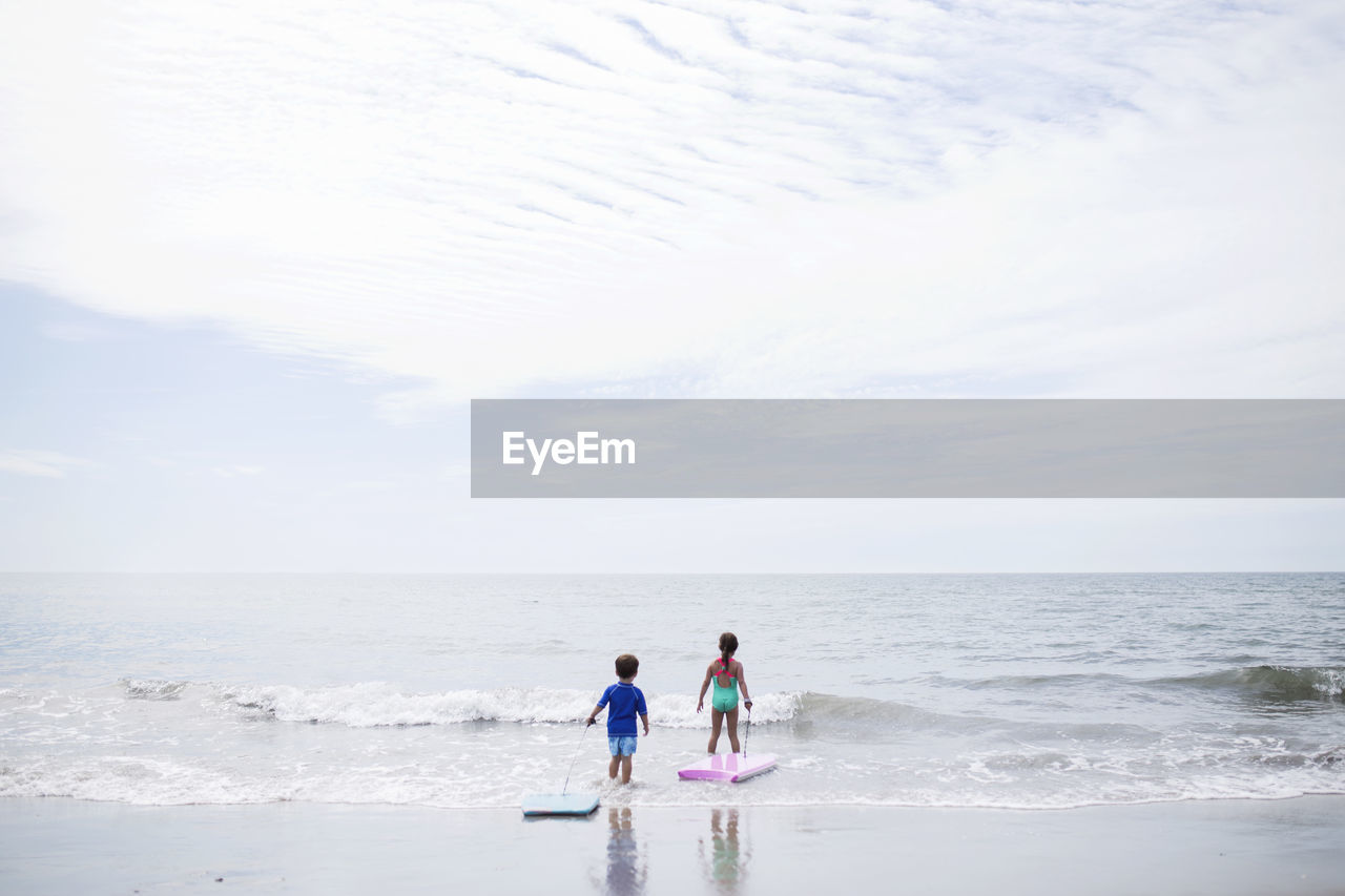 Scenic view of children wading into sea against sky
