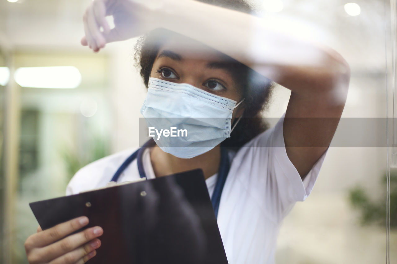 Nurse wearing mask looking away through glass