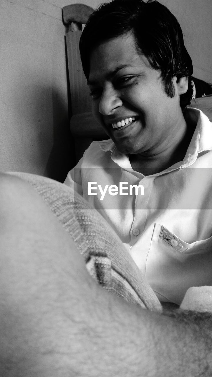 PORTRAIT OF A SMILING YOUNG MAN SITTING AT HOME