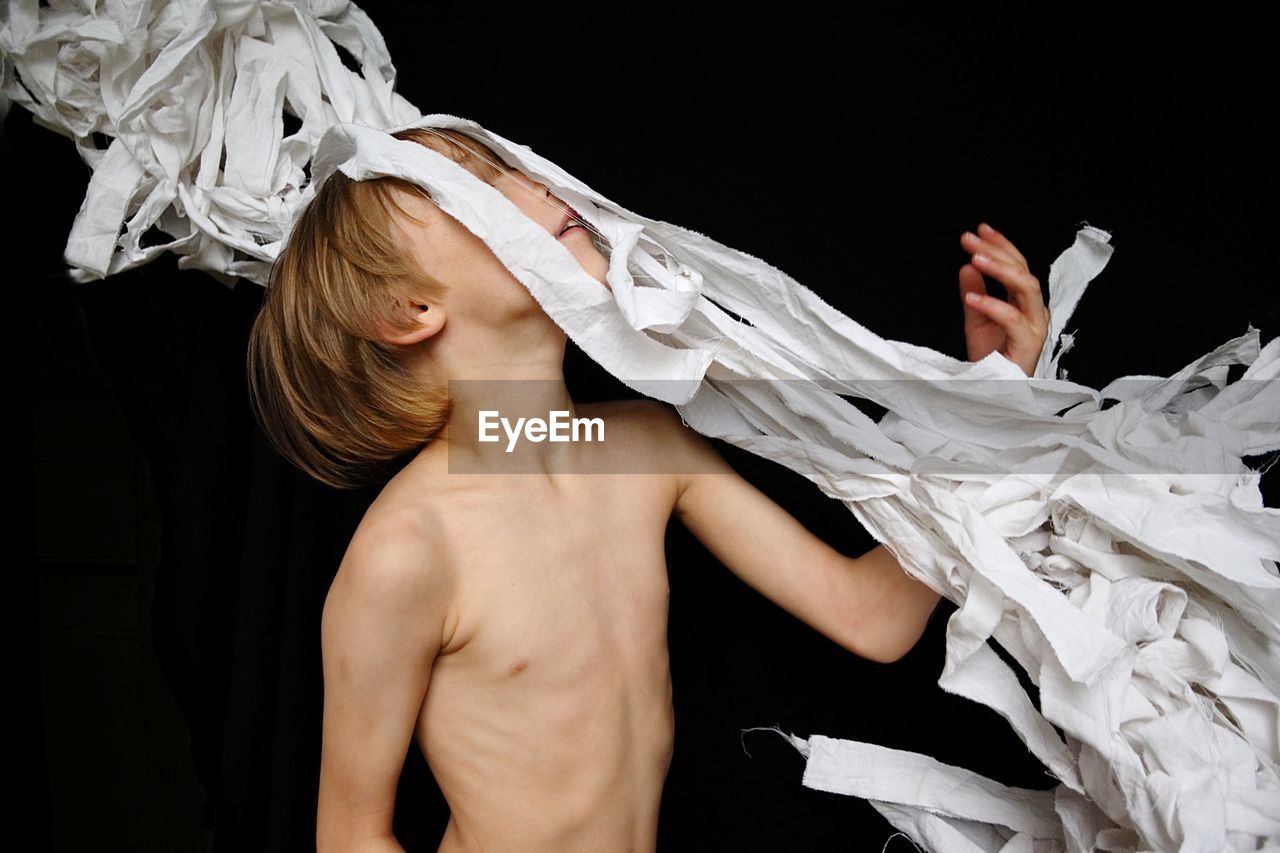 Shirtless boy throwing white fabric against black background