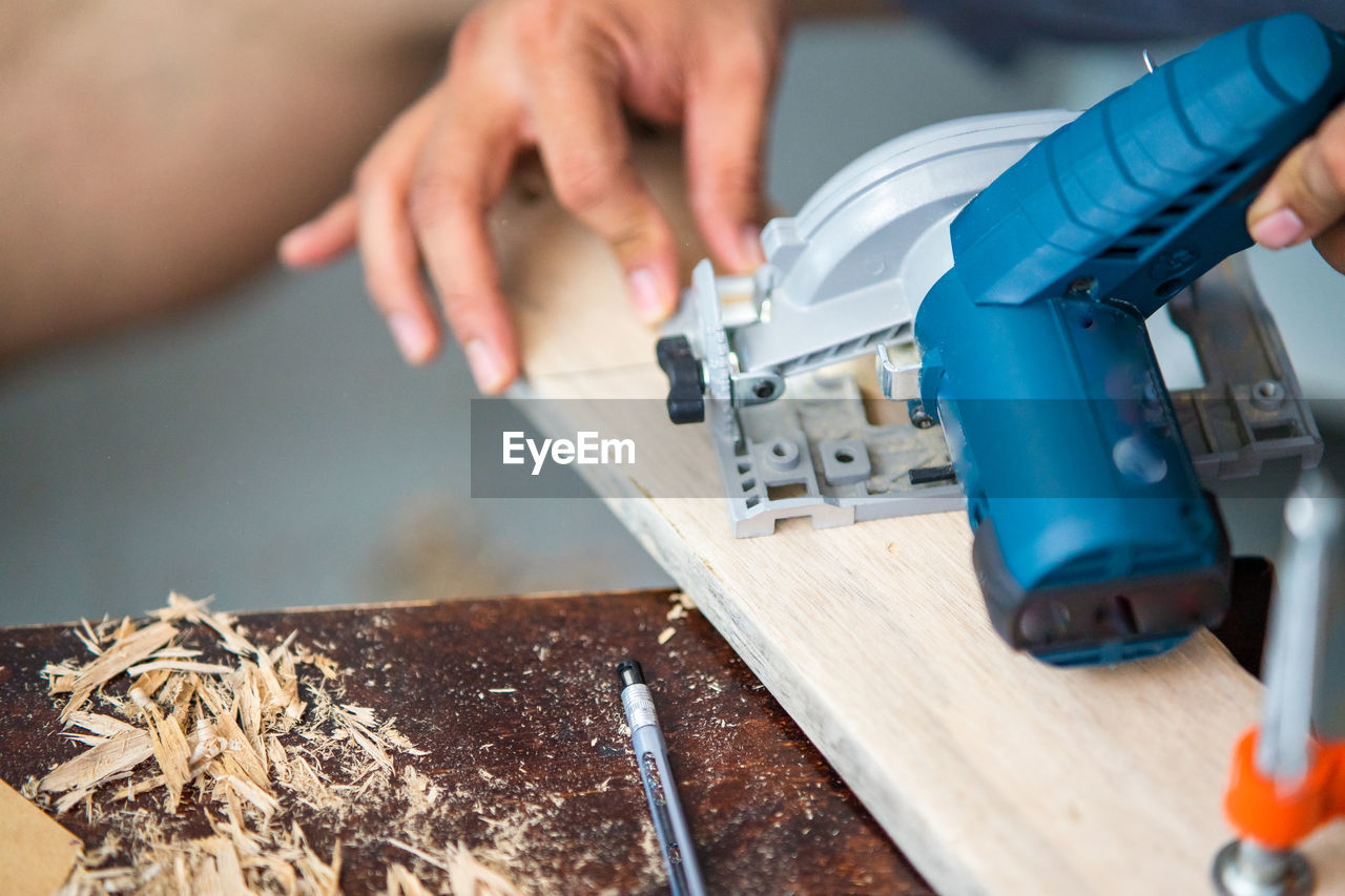 Close-up of man working on table with circular saw.