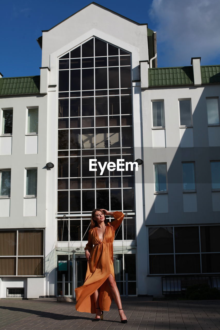 Glamorous urban photography, chic image of model in golden silk dress outdoors posing near building 