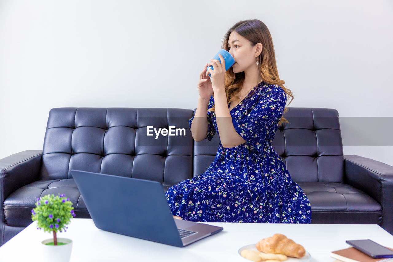 WOMAN LOOKING AWAY WHILE SITTING ON SOFA