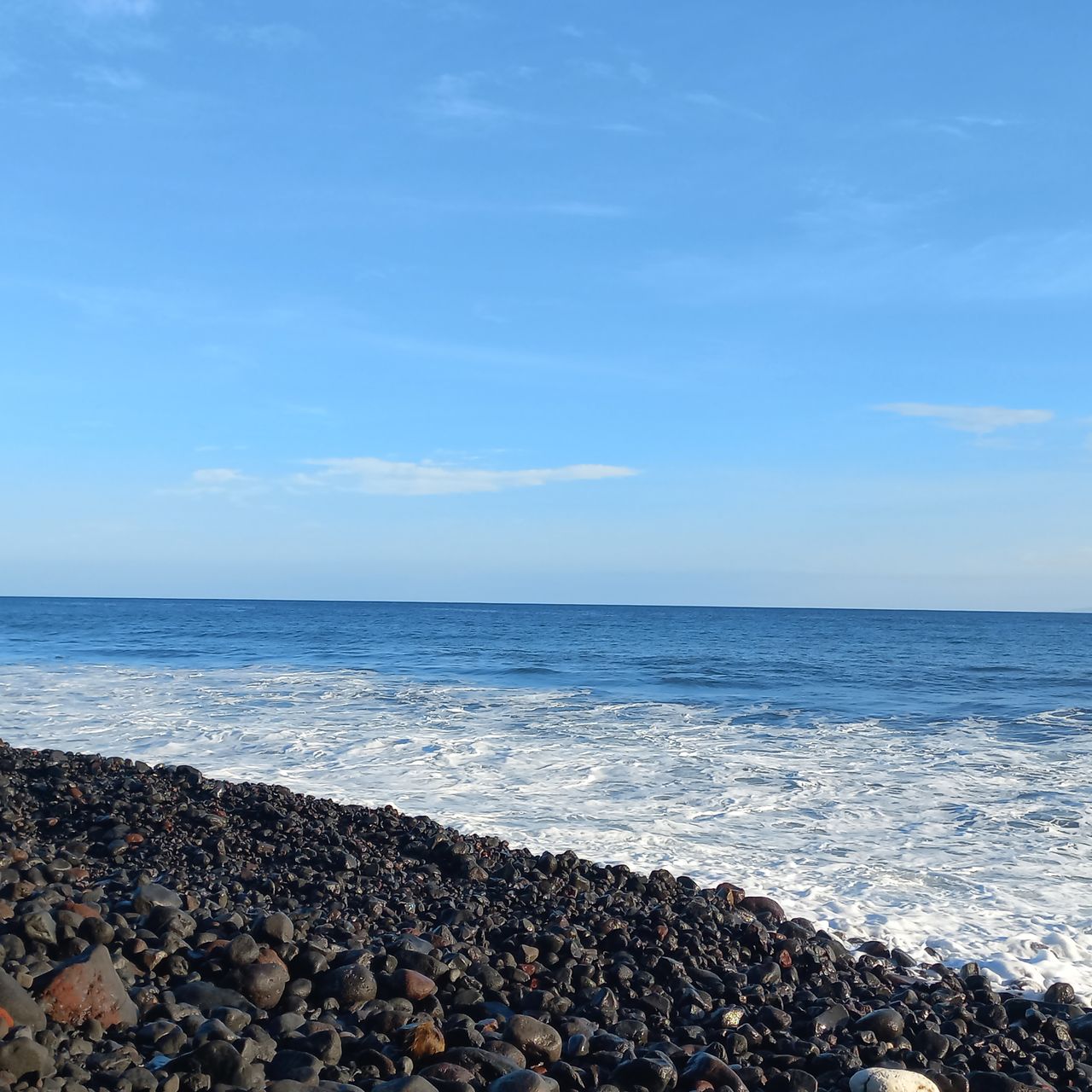 sea, water, sky, horizon over water, horizon, land, beach, shore, beauty in nature, ocean, rock, scenics - nature, body of water, nature, tranquility, wave, tranquil scene, coast, sand, blue, day, pebble, no people, cloud, stone, idyllic, outdoors, non-urban scene, motion, wind wave, sunlight