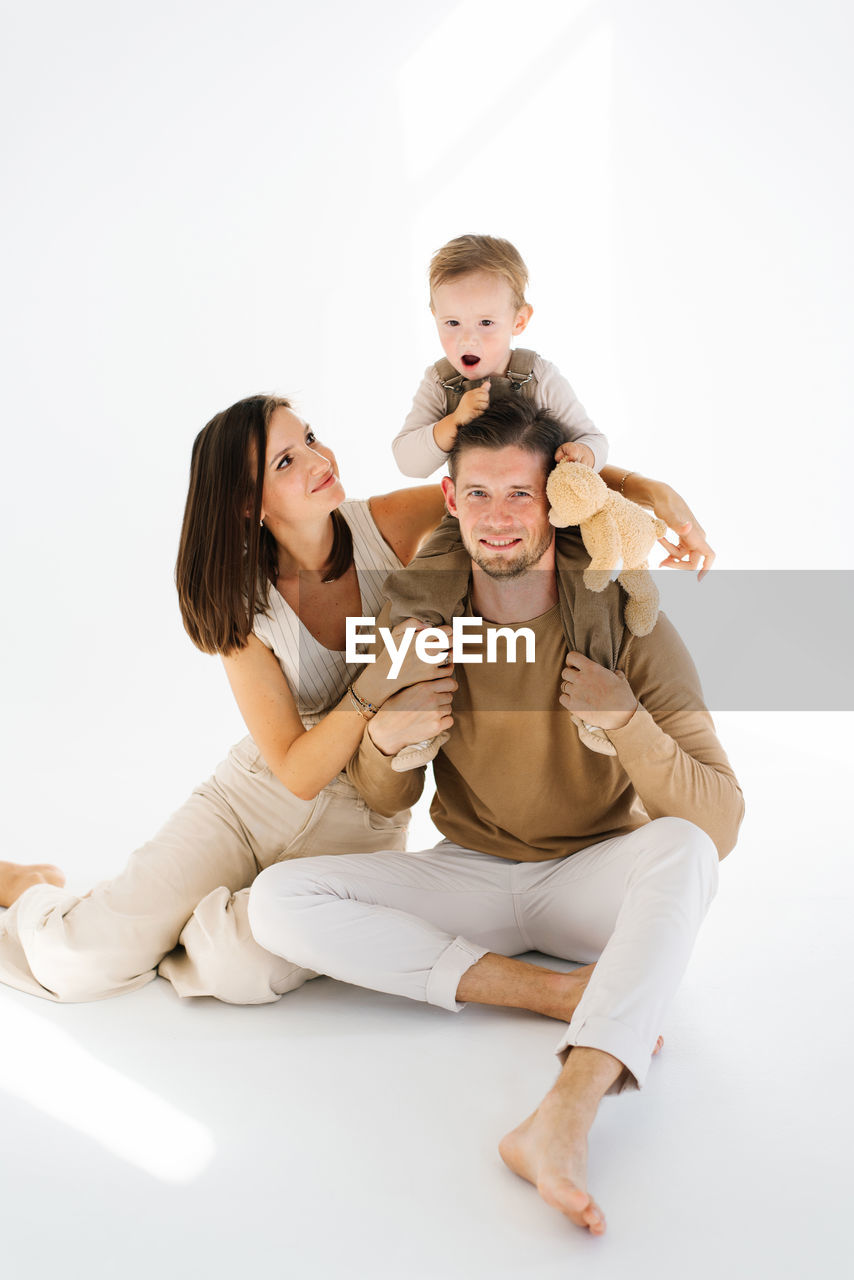 Mother and father hold their two year old son and a teddy bear in their arms