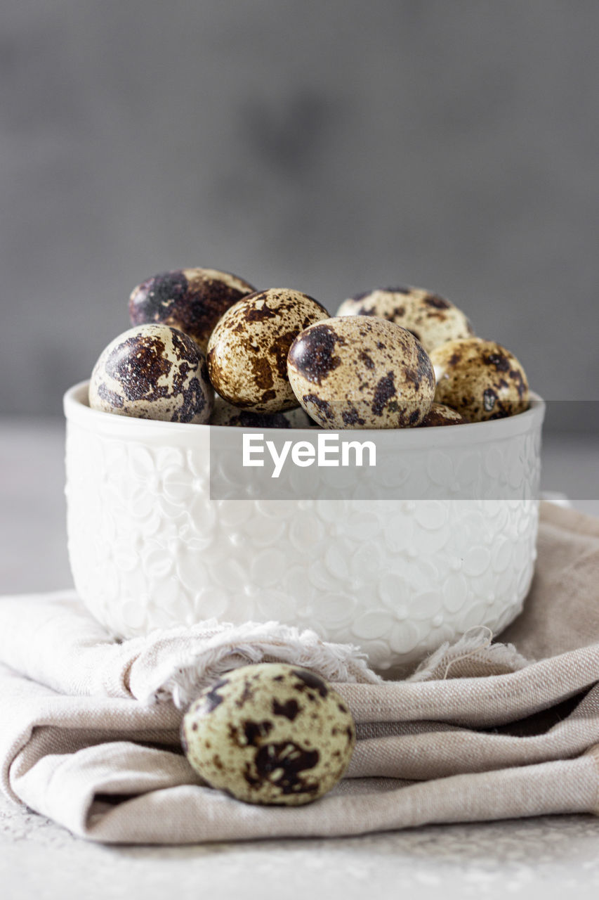 White ceramic bowl with quail eggs, light grey stone background. 