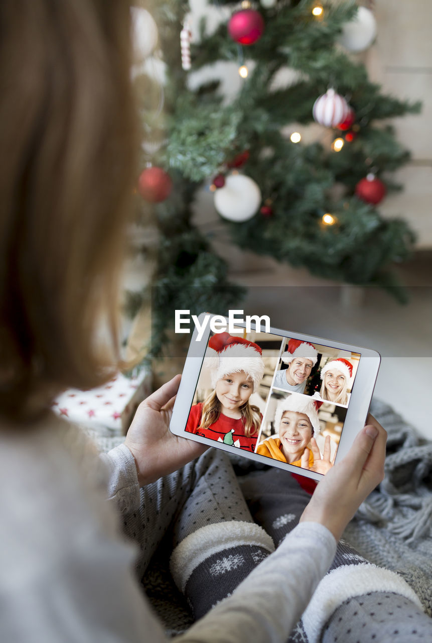 Girl video conferencing while holding digital tablet by christmas tree