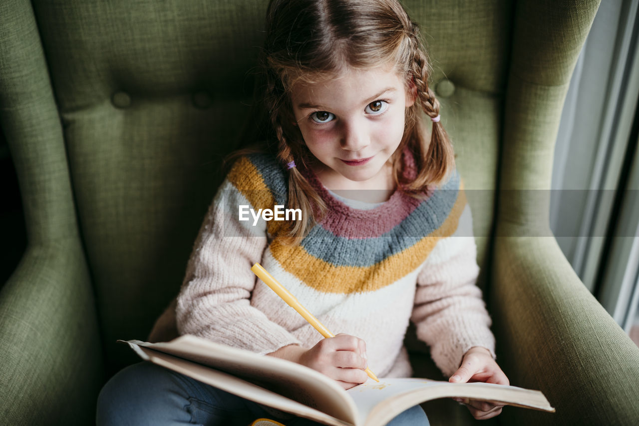 Cute girl doing homework while sitting on chair at home