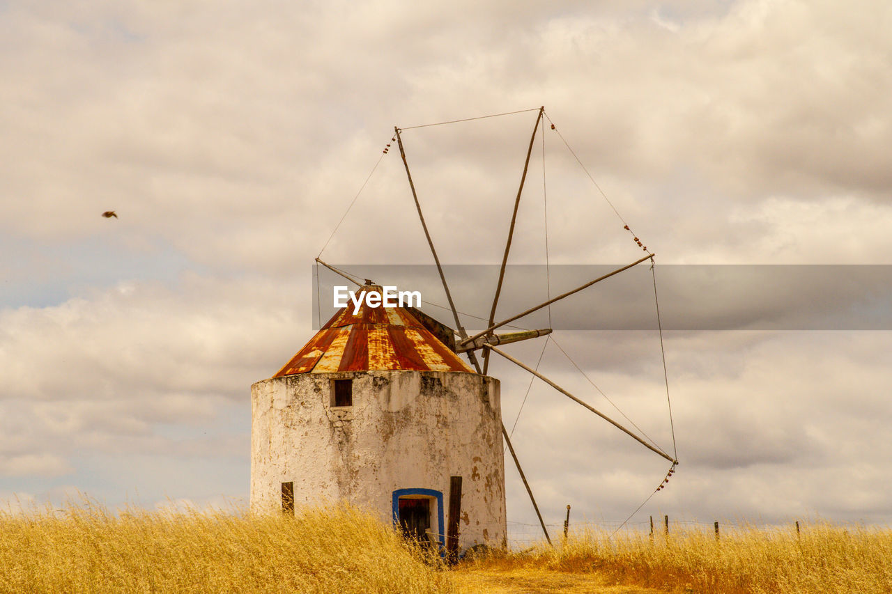 TRADITIONAL WINDMILL ON FIELD BY BUILDING AGAINST SKY