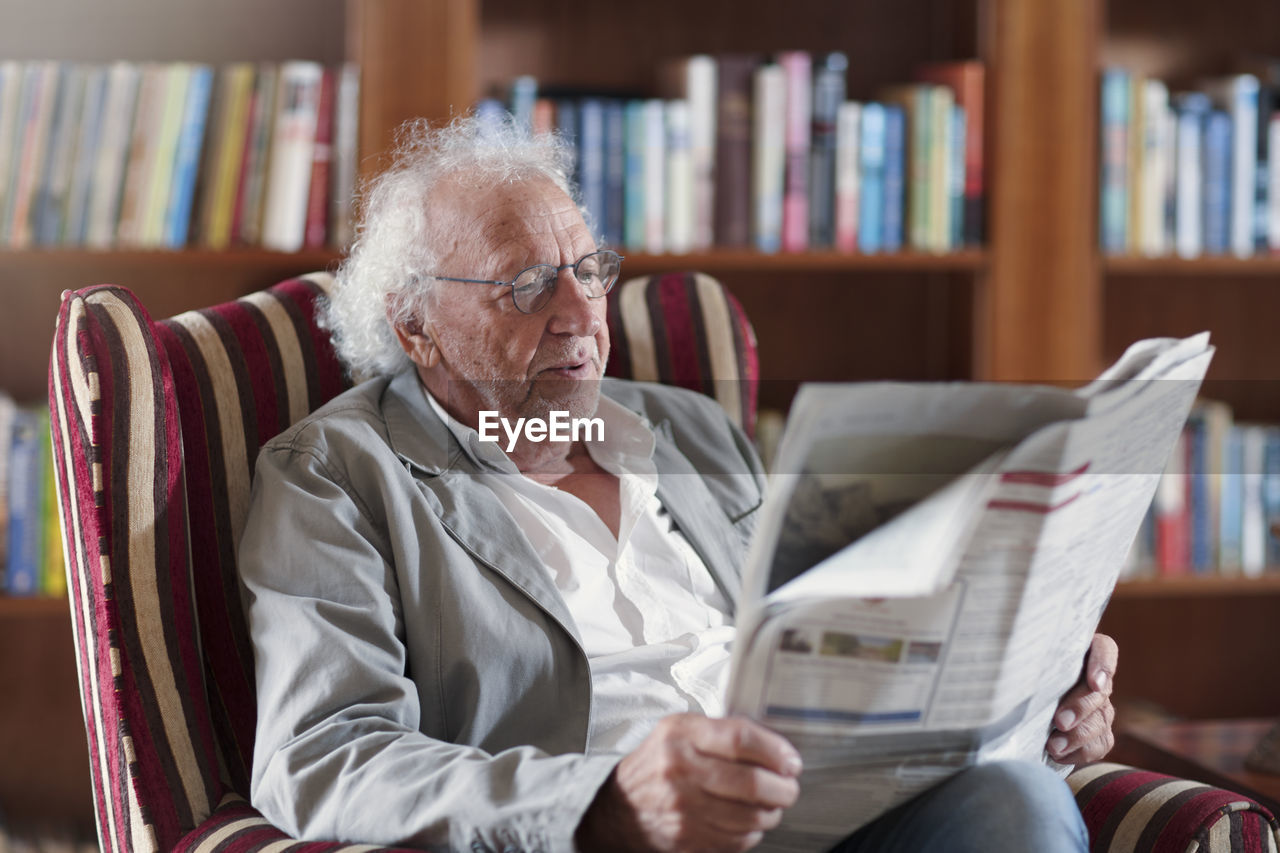 Senior man sitting in library, reading newpaper