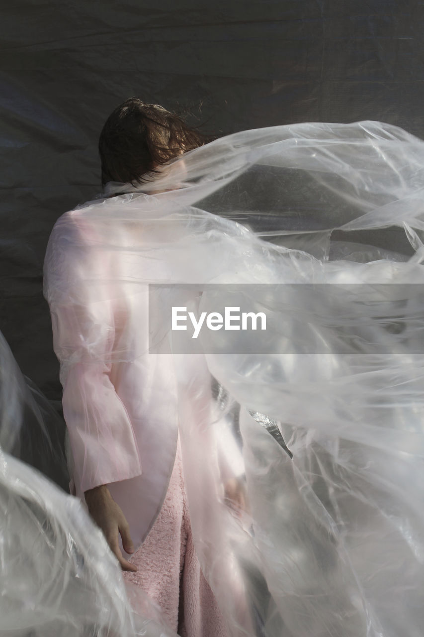 Man wrapped in plastic while standing against wall