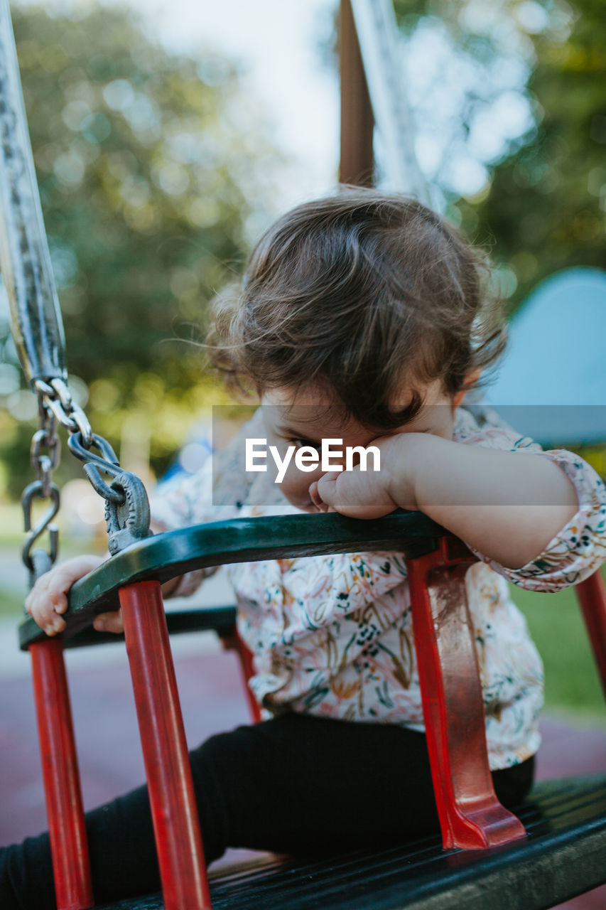 Portrait of baby girl sitting on swing at park