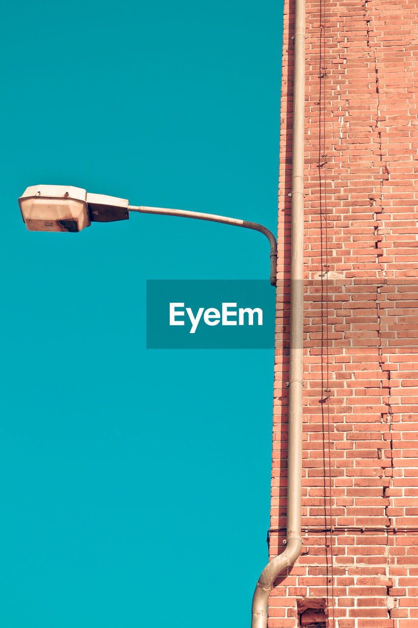 Low angle view of street light on brick wall against clear blue sky