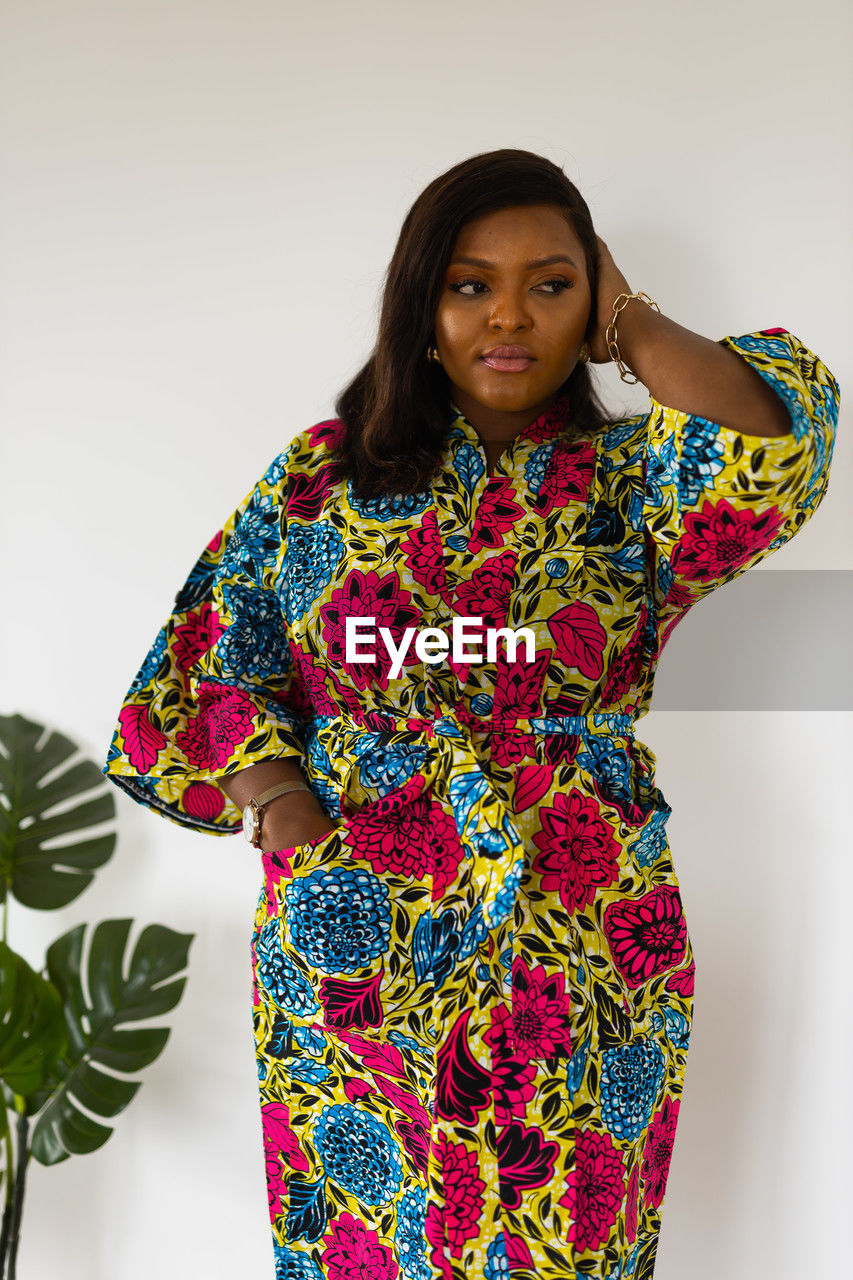 one person, sleeve, portrait, studio shot, women, indoors, adult, clothing, standing, looking at camera, pattern, dress, three quarter length, white background, fashion, young adult, front view, multi colored, floral pattern, waist up, hairstyle, smiling, female, emotion, outerwear, spring, textile, black hair, photo shoot