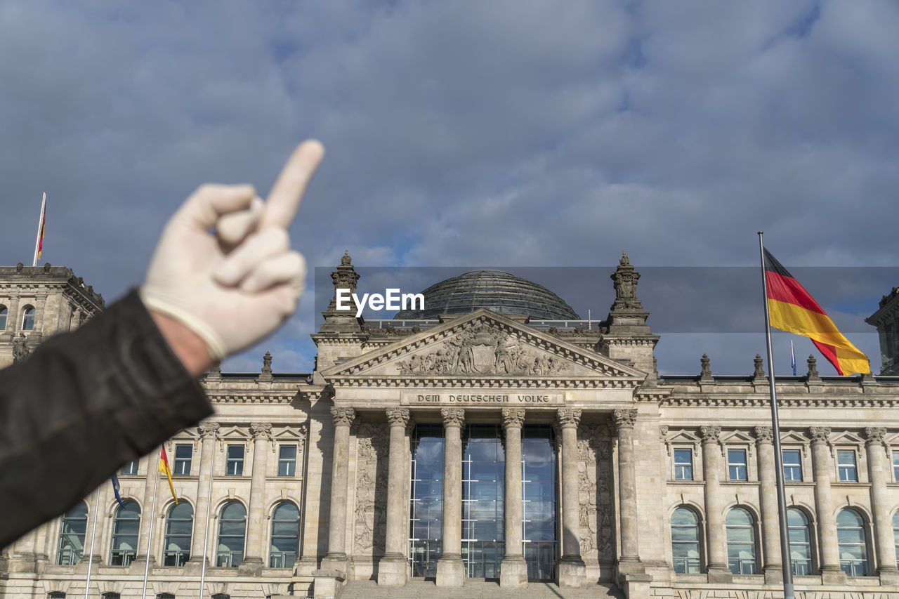 Hand with latex gloves giving german bundestag in berlin the middle finger. selective focus