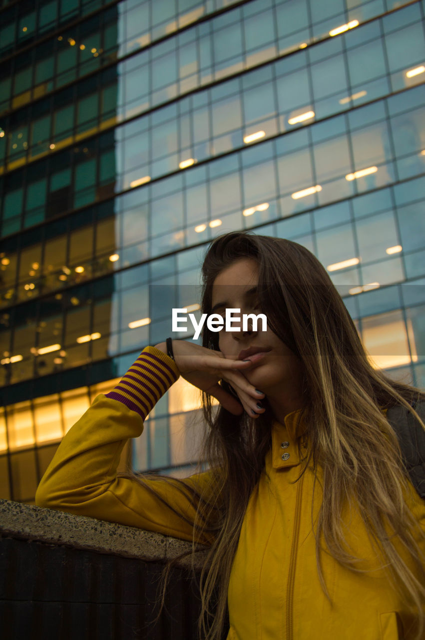 BEAUTIFUL YOUNG WOMAN STANDING BY ILLUMINATED BUILDING