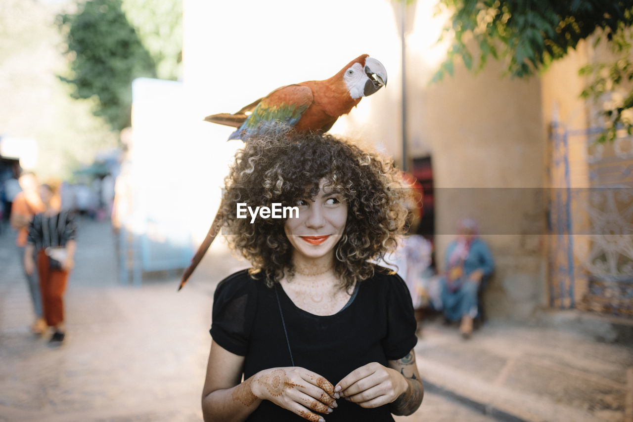Young woman with macaw on head in city
