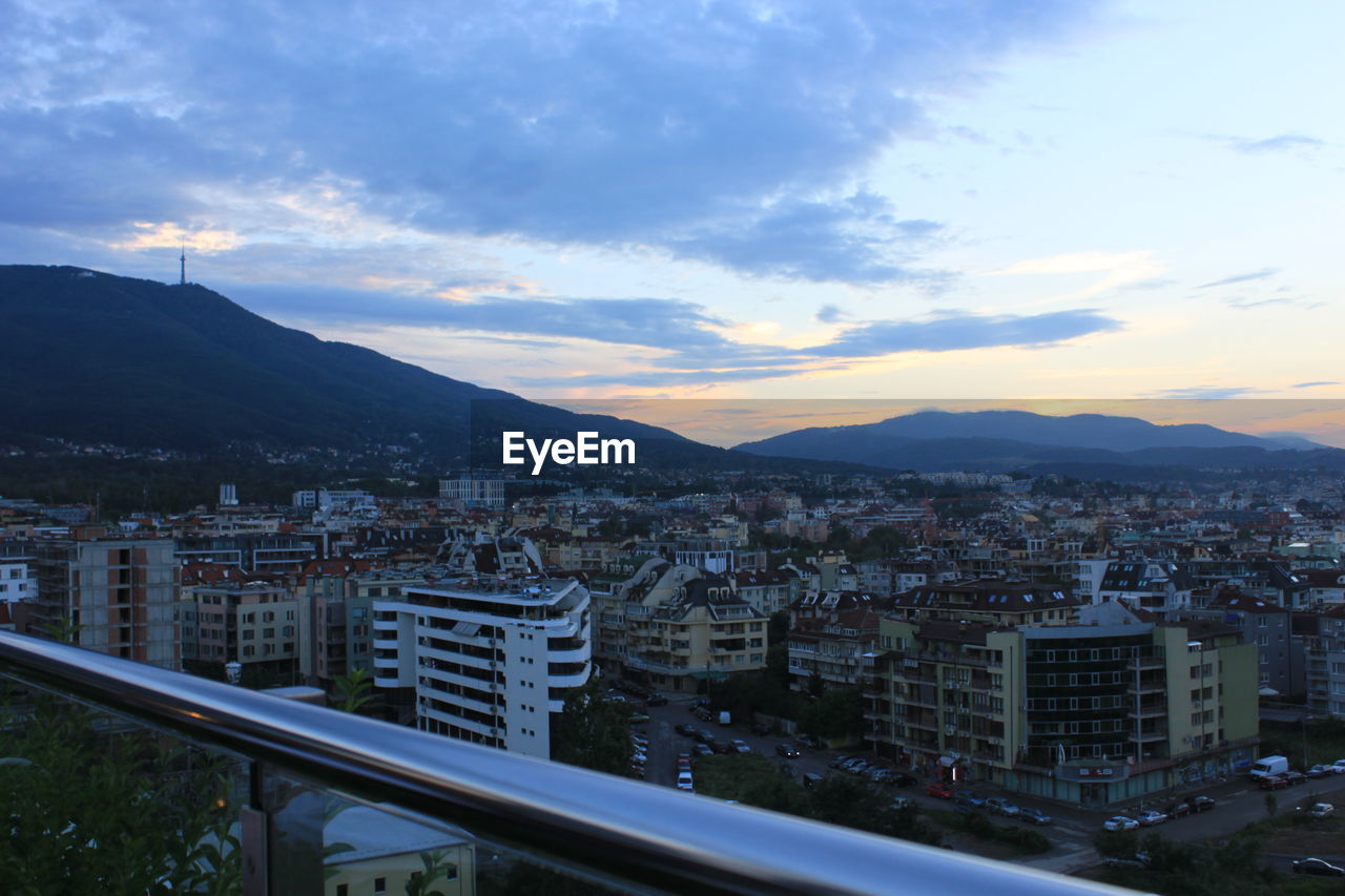 HIGH ANGLE VIEW OF ROAD BY BUILDINGS AGAINST SKY