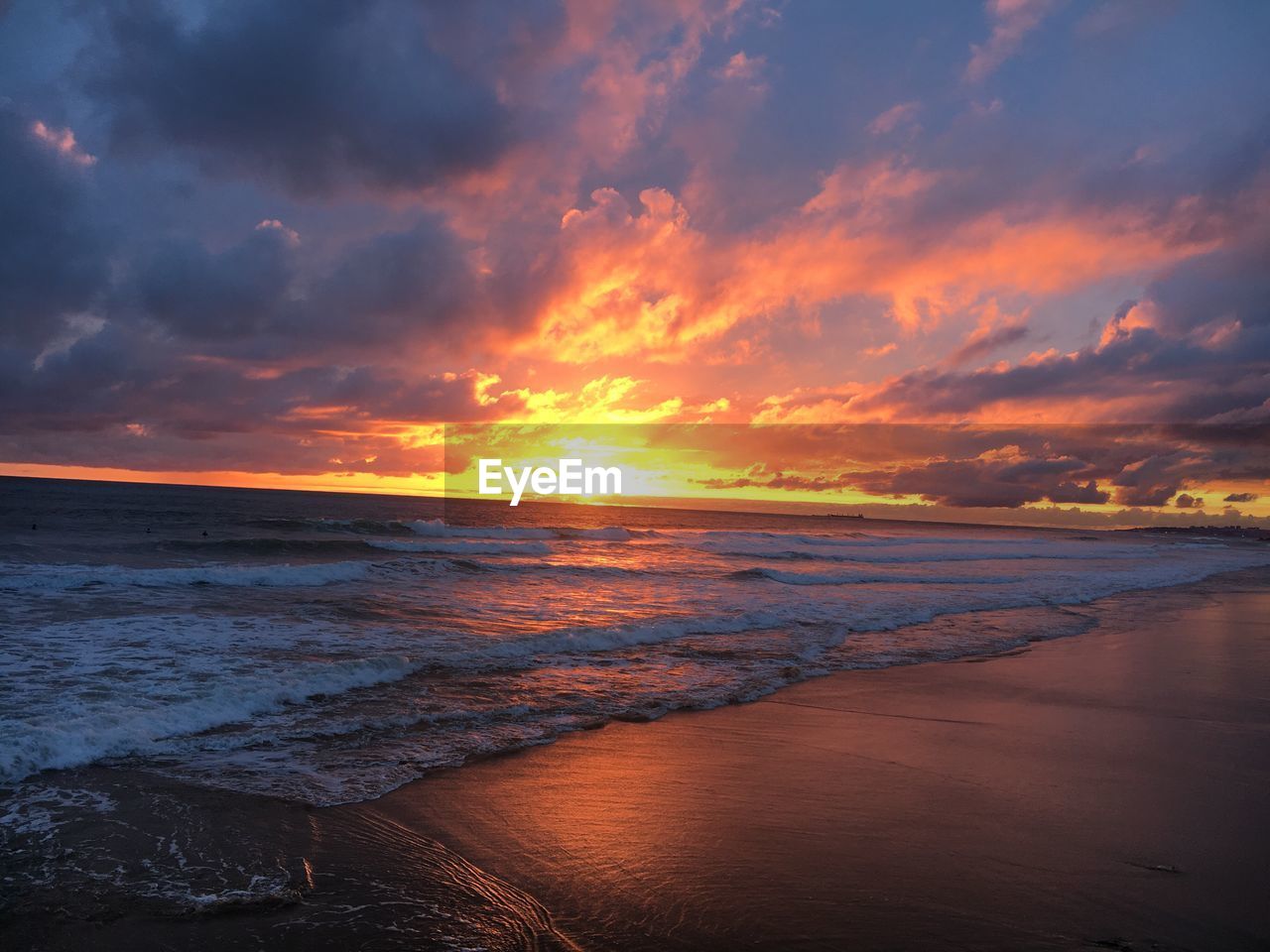 Scenic view of beach against dramatic sky during sunset