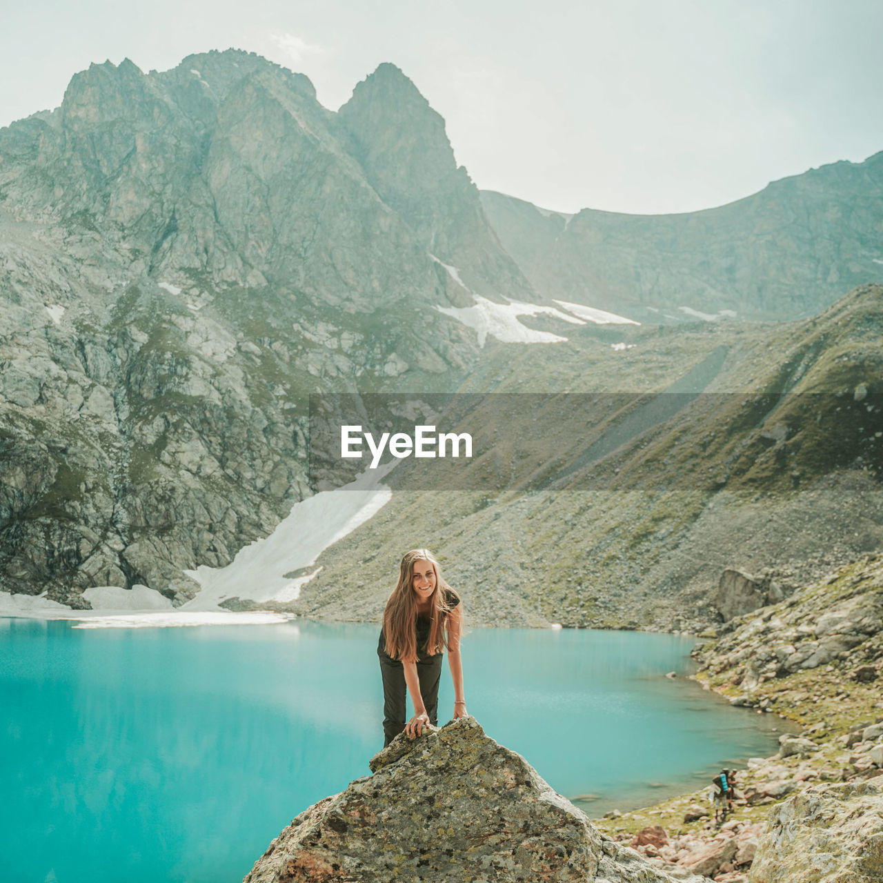 WOMAN STANDING ON ROCK BY MOUNTAIN AGAINST SKY