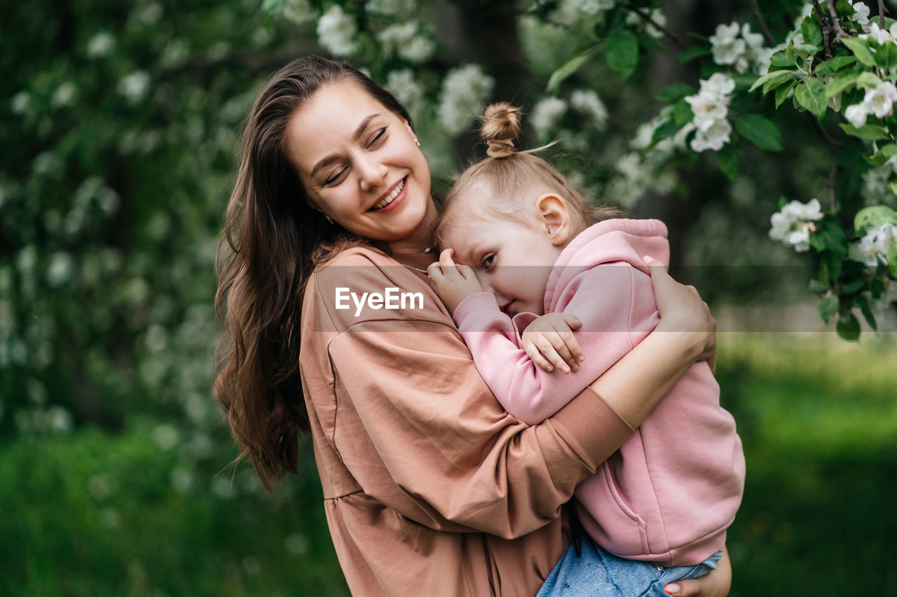 Young mother with her daughter in her arms in a blooming apple orchard