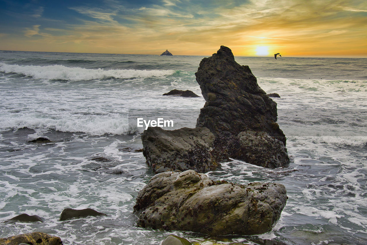 ROCK FORMATION ON SEA SHORE AGAINST SKY DURING SUNSET