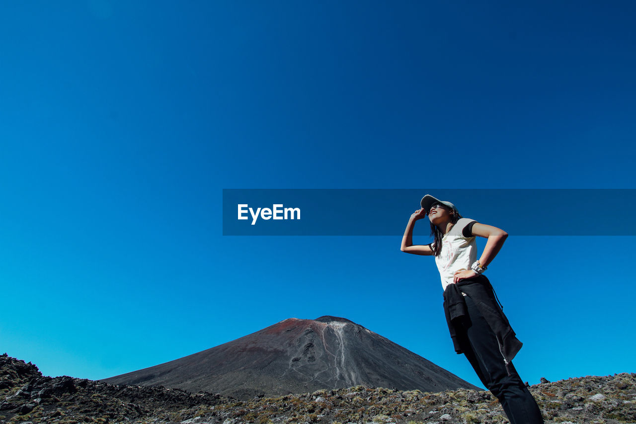 Low angle view of woman standing against clear blue sky