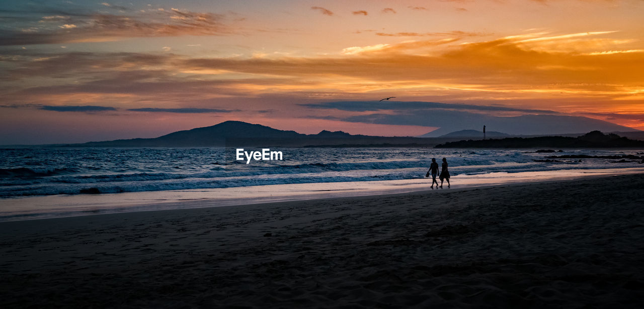 Silhouette people on beach against sky during sunset