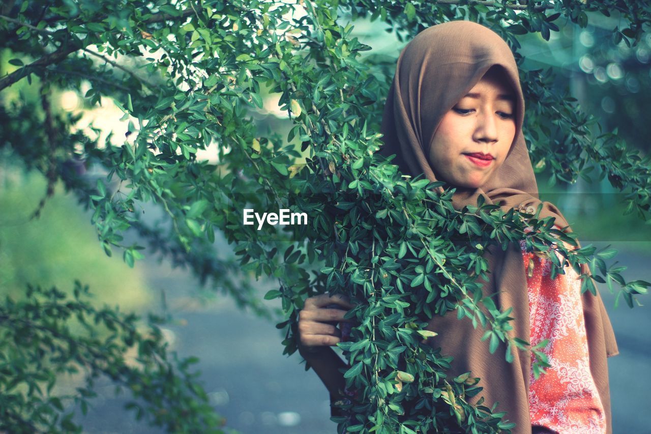Beautiful woman wearing hijab standing by plants