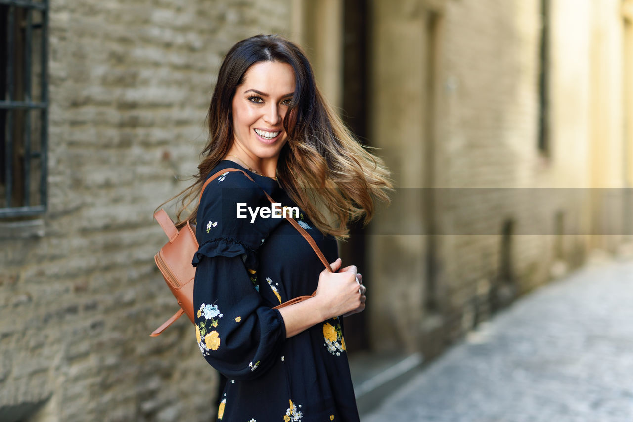 Portrait of smiling young woman standing by buildings outdoors