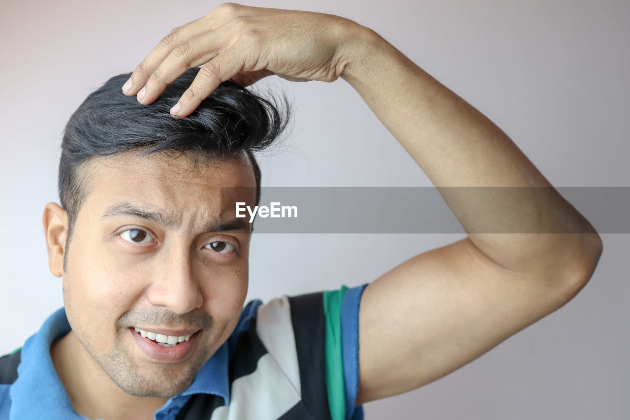 Close-up portrait of smiling man with hand in hair against gray background