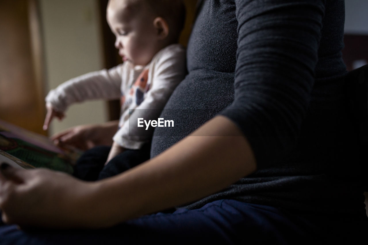 Midsection of pregnant woman showing picture book to daughter while sitting at home