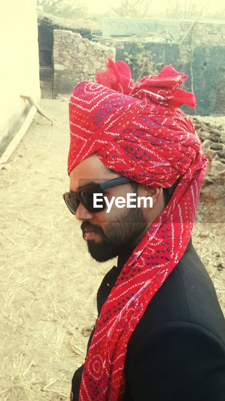 CLOSE-UP OF MAN WEARING SUNGLASSES AGAINST RED WALL